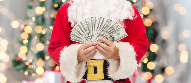 Natale, vacanze, vincita, valuta e concetto di persone - primo piano di Babbo Natale con soldi in dollari su sfondo di luci ad albero