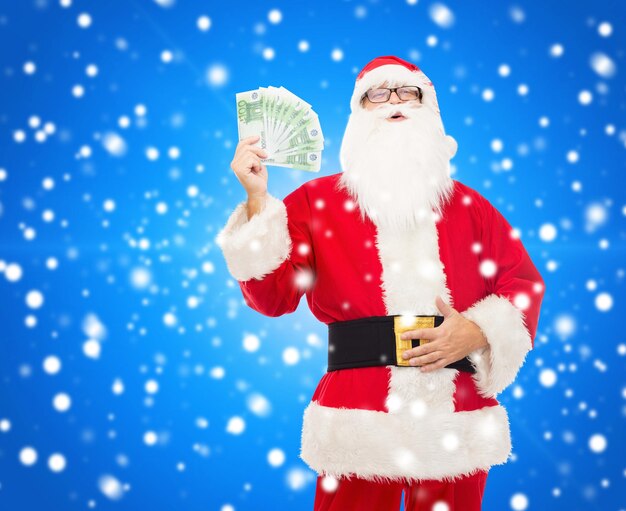 Natale, vacanze, vincita, valuta e concetto di persone - uomo in costume di babbo natale con soldi in euro su sfondo blu innevato