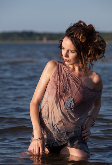 Natura, bellezza, gioventù e concetto di stile di vita sano. Attraente giovane donna seminuda in una muta in posa sullo sfondo del mare. Luce della sera con ombre profonde e cambiamento di colore