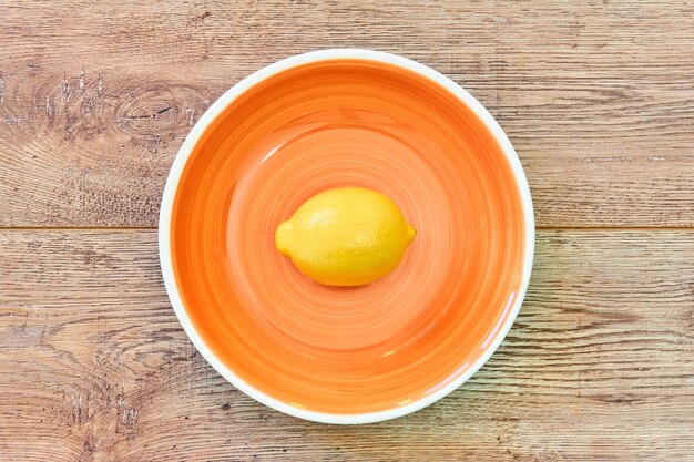 Natura morta a colori - limone giallo su un piatto arancione su un ripiano del tavolo in legno