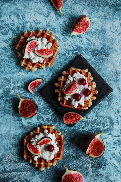 Natura morta ambientale di cialde di biscotti belghe con ricotta, fichi freschi e ciliegia. Sana colazione vegetariana.