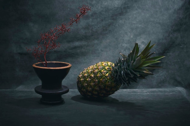 Natura morta con ananas e vaso marrone con un ramo