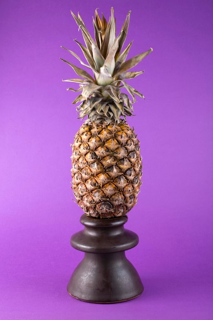 Natura morta con ananas su un supporto su sfondo viola