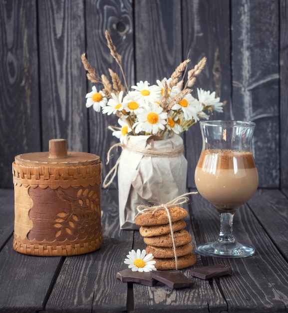 Natura morta con caffè freddo con latte e cioccolato con biscotti di farina d'avena e un bouquet di bellissime margherite in stile rustico su sfondo di legno