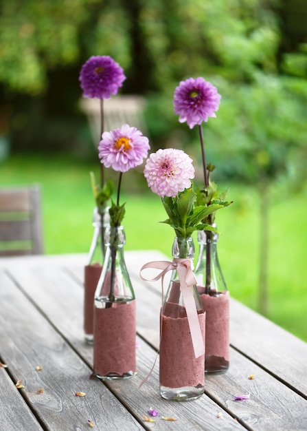 Natura morta con fiori di dalia rosa magenta viola rosa in bottiglie di vetro sul tavolo da giardino