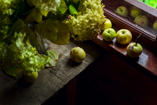 Natura morta con fiori di ortensia verde e un mazzo di mele verdi dalla finestra di una casa di campagna in legno