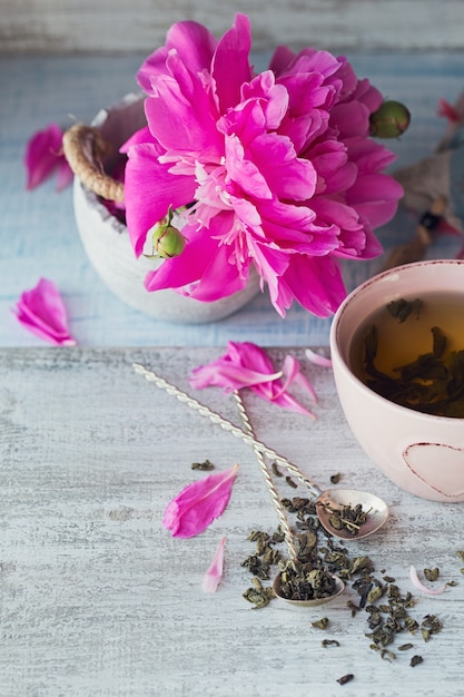 Natura morta con fiori di peonia rosa e una tazza di tè alle erbe o verde su fondo di legno rustico