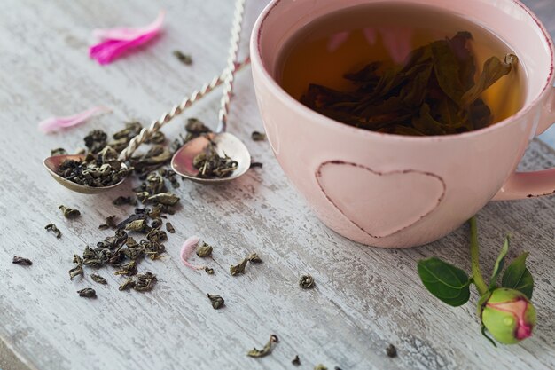 Natura morta con fiori di peonia rosa e una tazza di tè alle erbe o verde su fondo di legno rustico