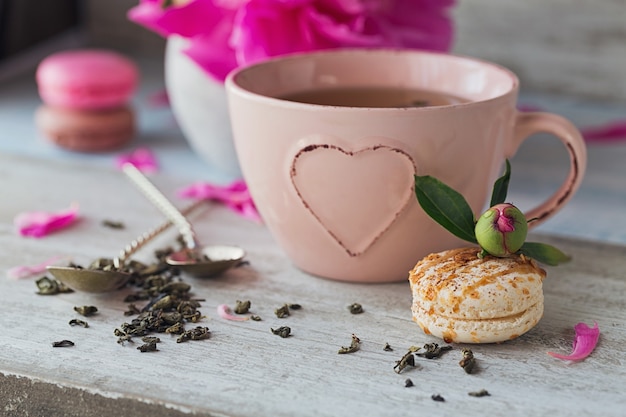 Natura morta con fiori di peonia rosa e una tazza di tè alle erbe o verde su fondo di legno rustico