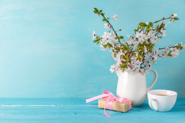 Natura morta con fiori di una bella primavera fiori di ciliegio, tazza di caffè e confezione regalo sul tavolo di legno blu con spazio di copia