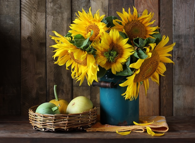 Natura morta con il mazzo dei girasoli in una vecchia merce nel carrello blu delle zucche e delle zucche, stile rustico.