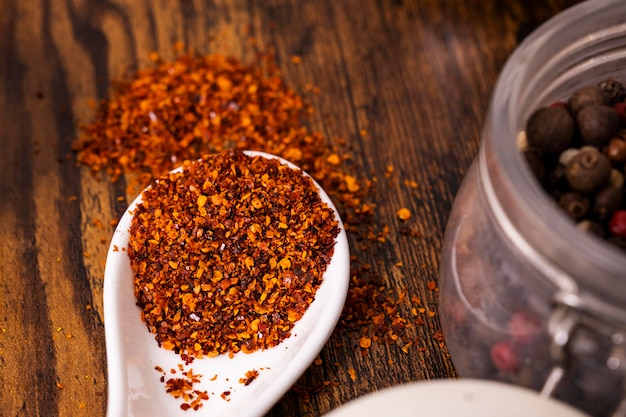 Natura morta con un cucchiaio bianco pieno di peperoncino grattugiato sul tavolo marrone