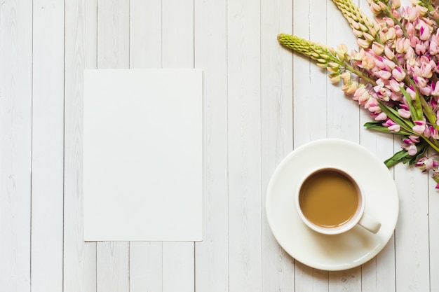 Natura morta con una tazza di caffè e fiori di lupino Blocco note su un tavolo di legno chiaro. Copia spazio