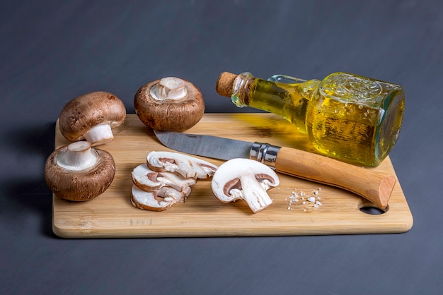 Natura morta di funghi champignon reali su un tagliere con coltello e una bottiglia con vista ad alto angolo di olio d'oliva