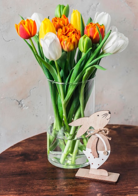 Natura morta di Pasqua Bouquet di tulipani colorati in un vaso di vetro e una decorazione di coniglietto di Pasqua in legno sul tavolo