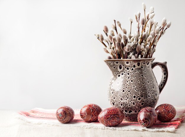 Natura morta di Pasqua con rami Pysanka e salice in brocca in ceramica sul tradizionale panno ucraino. Uova di Pasqua decorate, tradizionali per la cultura dell'Europa orientale