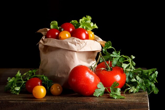 Natura morta di pomodori, aglio e prezzemolo su tavole di legno. Su uno sfondo nero.