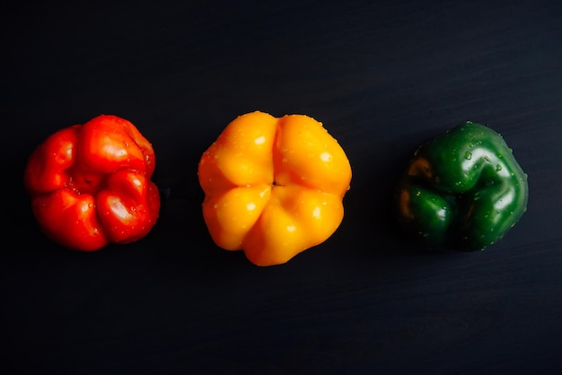 Natura morta di tre peperoni bulgari dolci su fondo di legno nero, primo piano. Paprica fresca matura di colore rosso, giallo e verde. Disposizione piatta. Vista dall'alto.