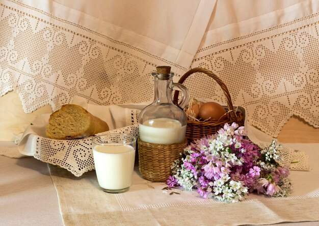 Natura morta Il cesto con uova e fiori selvatici latte e pane sul primo piano del tavolo