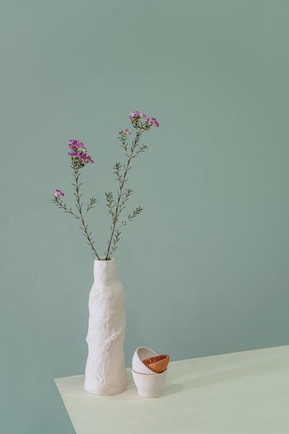 Natura morta minimalista di piatti in ceramica con fiori sul tavolo sullo sfondo turchese