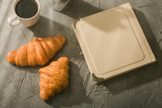 Natura morta per una piacevole tazza di caffè turco mattutino e croissant con libro sul concetto di pausa pranzo al tavolo