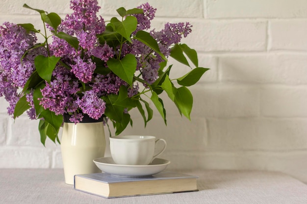 Natura morta primavera estate Vaso con bouquet di lillà sulla tovagliaUna tazza di caffè o tè e un libro da leggere