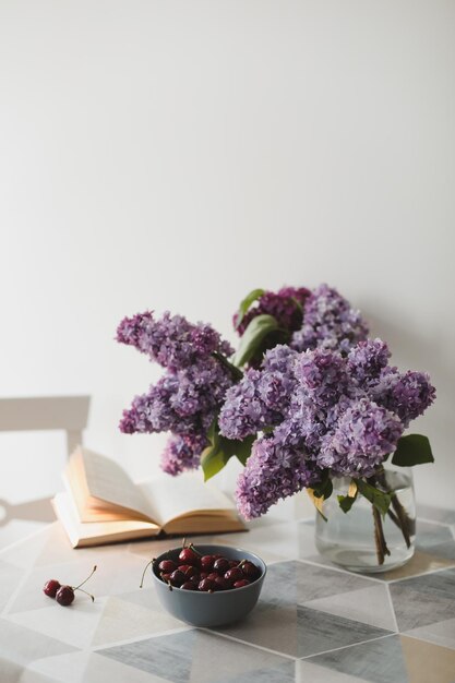 Natura morta romantica con un libro aperto fiori lilla e ciliegie su un tavolo
