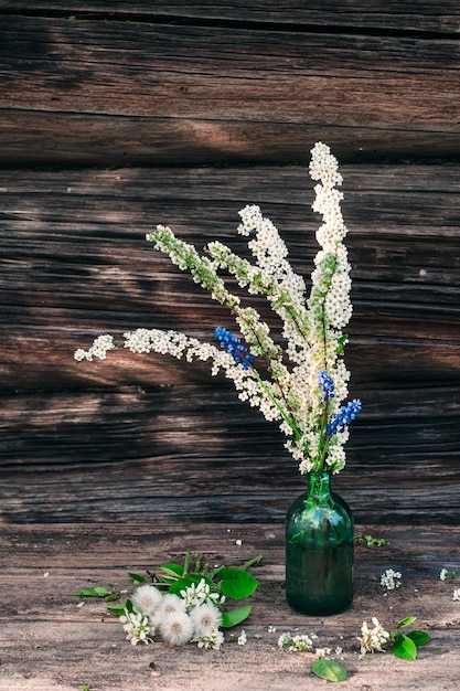 Natura morta rustica. Una bottiglia di vetro con fiori primaverili sullo sfondo del muro di una casa di paese.