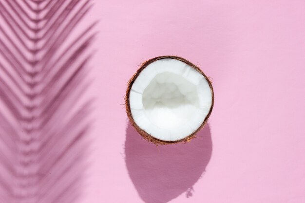 Natura morta tropicale minimalista. Due metà di cocco tritato con ombre di foglie di palma su sfondo rosa. Concetto di moda creativa.