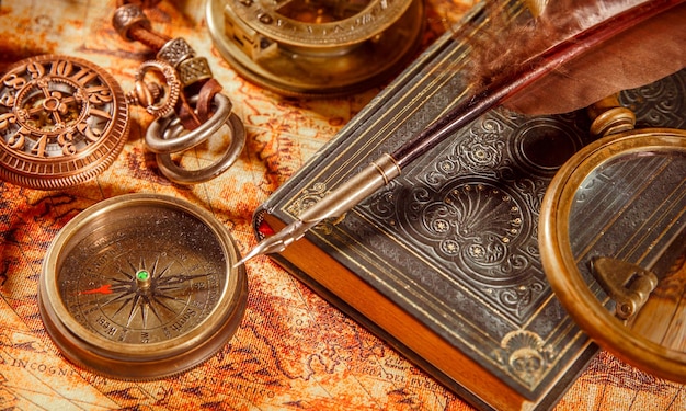 Natura morta vintage - lente d'ingrandimento, orologio da tasca, vecchio libro e penna d'oca che giace su una vecchia mappa nel 1565.