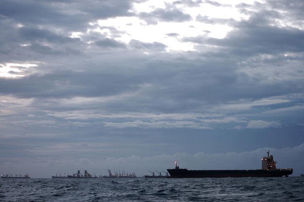 Nave mercantile galleggiante nell'oceano mare coda di attesa per il trasferimento di merci mentre tempesta di vento piovosa sera al tramonto tra Koh Loy e l'isola di Ko Sichang nella città di Sriracha a Chonburi Thailandia