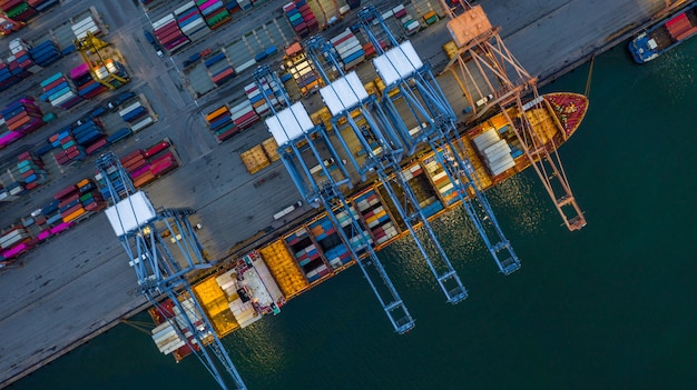 Nave porta-container di vista aerea che carica alla notte in porto industriale.