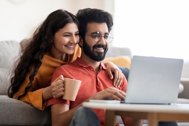 Navigare in internet giovane coppia indiana che si rilassa con il computer portatile e il caffè a casa