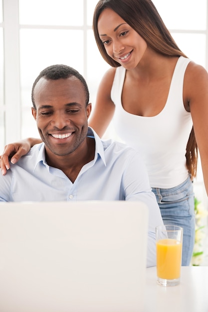 Navigare in rete insieme. Bella giovane coppia africana che guarda il laptop e sorride