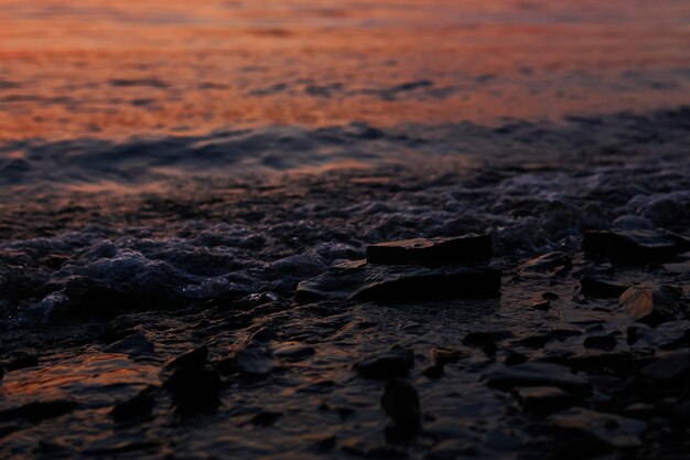 Navigare sulla spiaggia rocciosa al tramonto in primo piano con il riflesso del tramonto sulle onde