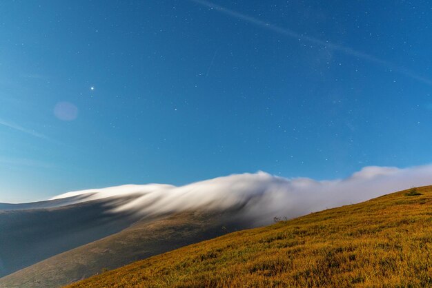 Nebbia densa e soffice che copre il picco della montagna con una foresta di conifere verdi sotto il cielo blu di notte luminosa nella vista serale autunnale