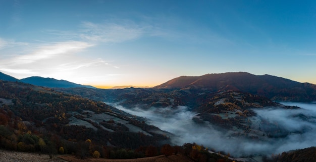 Nebbia fitta tra le cime delle alte montagne autunnali all'alba