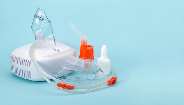 Nebulizzatore a compressore e maschere respiratorie su sfondo blu posto vuoto a destra Set di apparecchiature mediche per terapia inalatoria per asma e malattie respiratorie