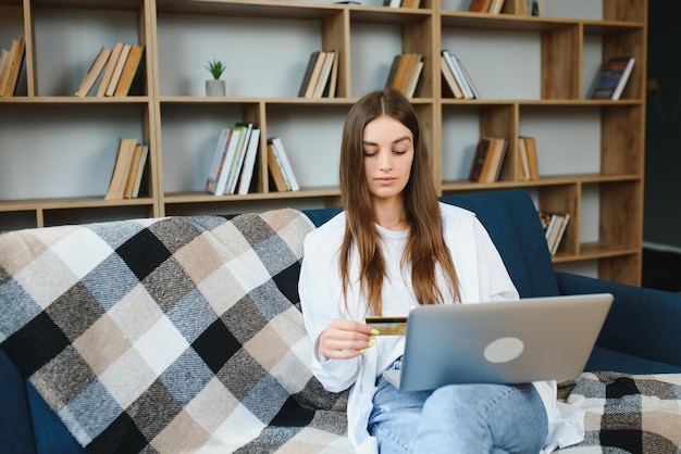 Negozio online Ragazza felice che fa shopping via internet utilizzando laptop e carta di credito seduta sul copyspace del divano