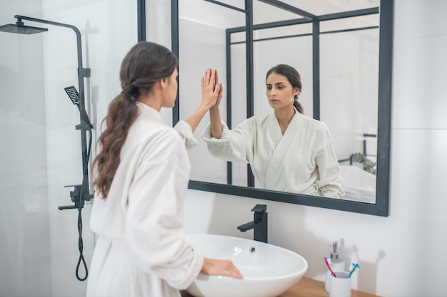 Nel bagno. Una ragazza dai capelli scuri in un accappatoio bianco in bagno