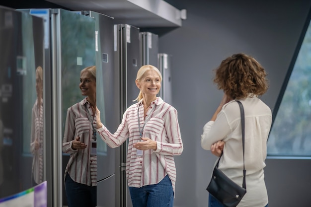 Nel megastore. Assistente di vendita in camicia a righe che mostra un nuovo frigorifero al cliente femminile