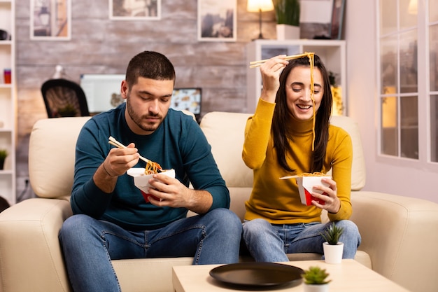 Nel moderno e accogliente soggiorno, la coppia si sta godendo i noodles da asporto mentre guarda la TV comodamente sul divano