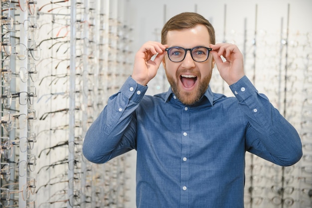 Nel negozio di ottica Ritratto di un cliente maschio che tiene in mano e indossa diversi occhiali scegliendo e provando nuovi occhiali nel negozio di ottica Uomo che sceglie il telaio per la correzione della vista in primo piano