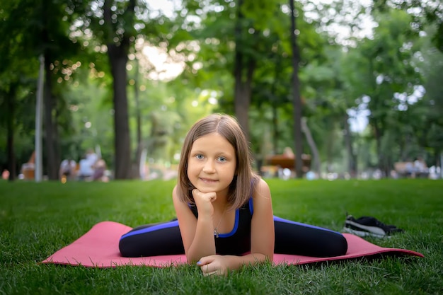 Nel parco una bambina esegue un elemento ranocchio facendo stretching su un materassino
