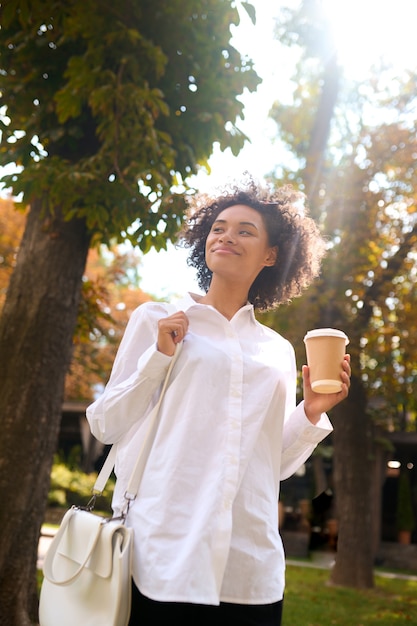 Nel parco. Una ragazza in camicia bianca con una tazza di caffè nel parco