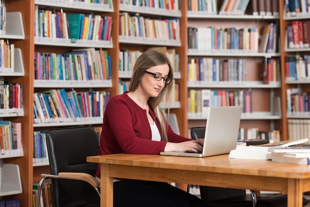 Nella biblioteca Bella studentessa con laptop e libri che lavorano in una biblioteca universitaria di scuola superiore Profondità di campo ridotta