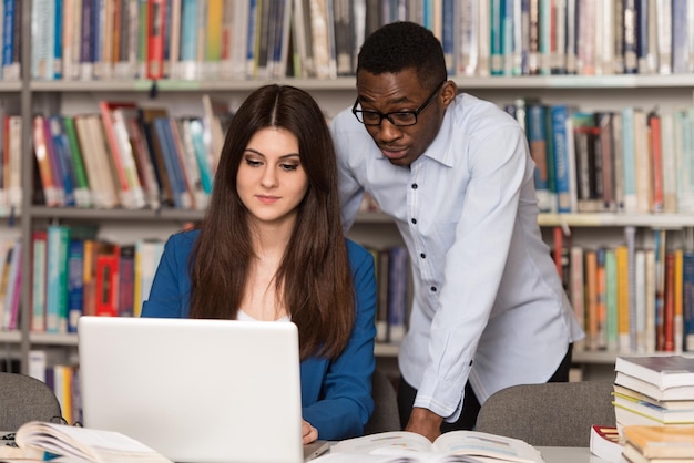 Nella biblioteca Bellissimi due studenti universitari con laptop e libri che lavorano in una biblioteca universitaria di scuola superiore Profondità di campo ridotta