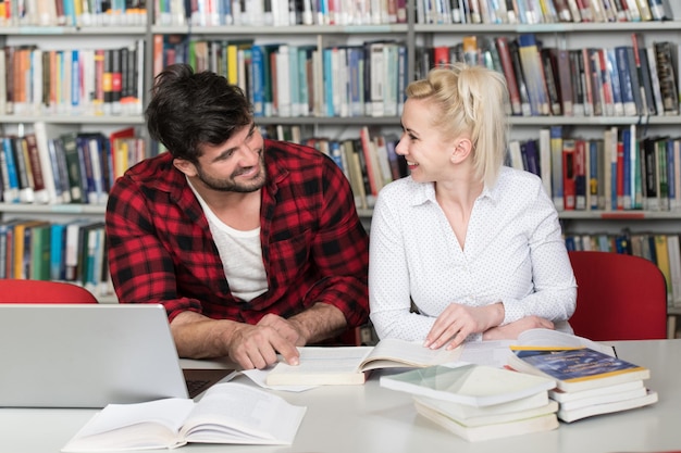 Nella biblioteca Bellissimi due studenti universitari con laptop e libri che lavorano in una biblioteca universitaria di scuola superiore