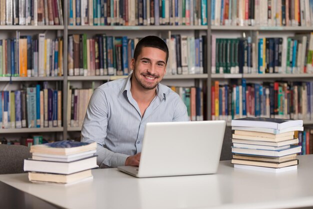 Nella biblioteca Studente maschio bello con il computer portatile ed i libri che lavorano in una profondità del campo poco profonda della biblioteca dell'università della High School