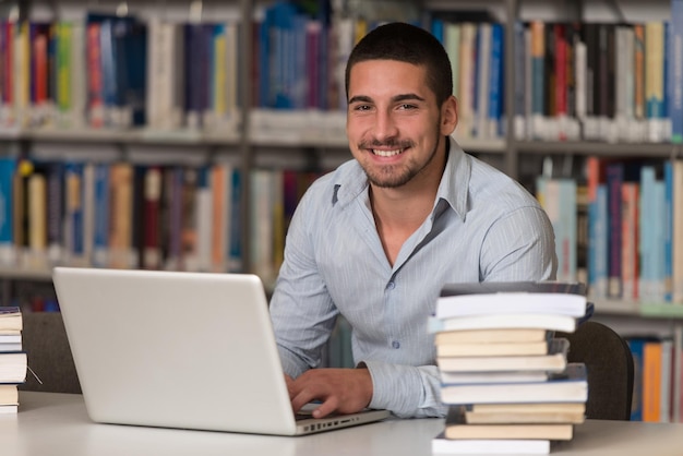 Nella biblioteca Studente maschio bello con il computer portatile ed i libri che lavorano in una profondità del campo poco profonda della biblioteca dell'università della High School